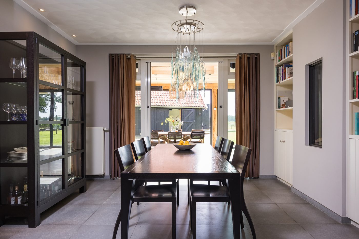 De eethoek met lange tafel en vitrinekast, met zicht naar de serre