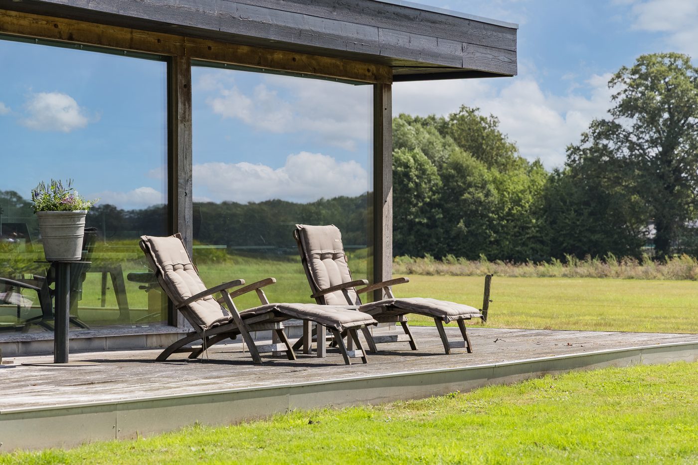 Het houten terras bij het kantoor, met ligstoelen en uitzicht over het weiland