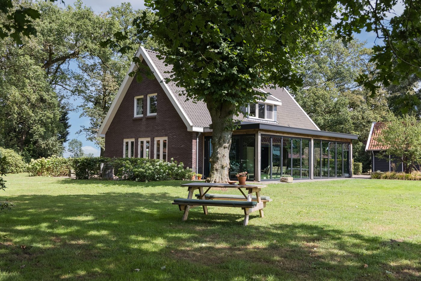 Het landhuis met serre achter een picknicktafel onder een grote boom