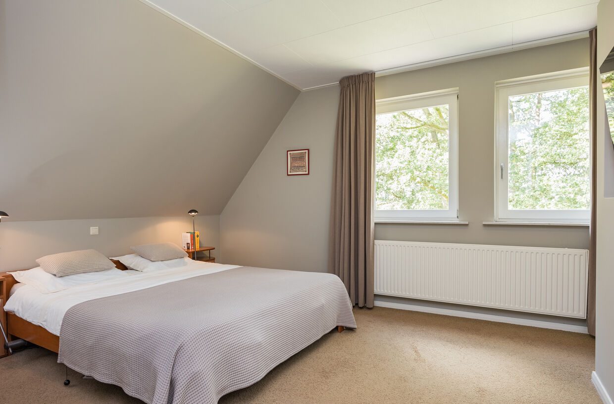 Een slaapkamer onder de schuine kap, met tweepersoonsbed en twee ramen