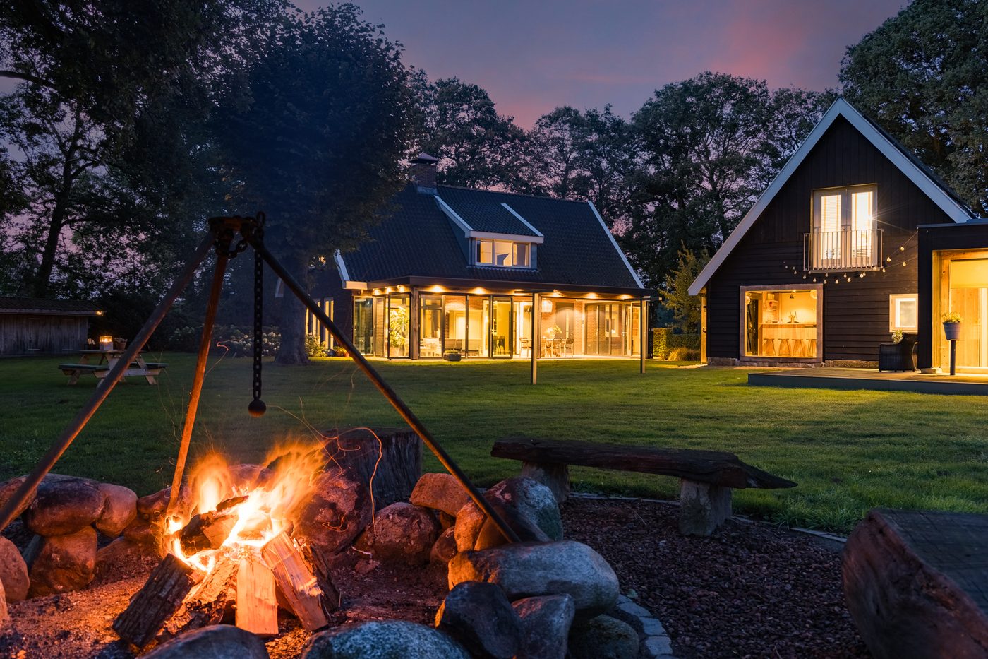 De vuurplaats bij avond, met het verlichte landhuis en kantoorgebouw op de achtergrond